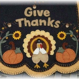 Może przedstawiać: Wisząca ozdoba ścienna z filcu z falistym brzegiem przedstawia indyka, dynie, słoneczniki i napis "Give Thanks".