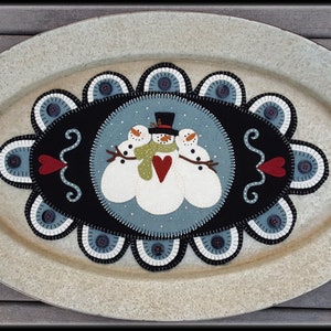 May include: A white oval metal serving tray with brown handles. The tray has a black felt center with a blue felt background. Three white felt snowmen with red hearts and a green scarf are in the center of the felt. The felt is surrounded by a white and blue scalloped border.