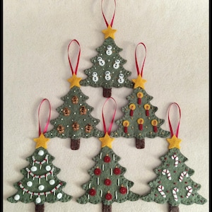 May include: A collection of six handmade felt Christmas tree ornaments. Each green tree has a brown trunk, a yellow star topper, and red ribbon for hanging. The trees are decorated with various festive designs, including snowmen, gingerbread men, candles, red ornaments, and candy canes.