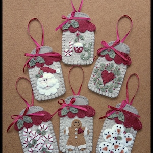 Può includere: Una collezione di ornamenti natalizi fatti a mano. Ogni ornamento è di forma rettangolare con un bordo smerlato, con disegni festivi come Babbo Natale, bastoncini di zucchero, pupazzi di neve e un omino di pan di zenzero. Sono in feltro con accenti rossi e verdi e un nastro.