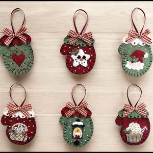 May include: Six felt Christmas decorations shaped like mittens with different festive designs. The ornaments are green and red with white accents and have red and white gingham bows.