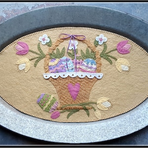 May include: A felt Easter table runner with a basket of colorful eggs, surrounded by tulips and flowers. The runner is displayed on a silver oval tray.