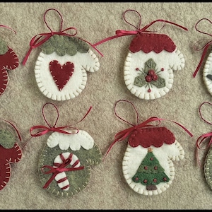 May include: Eight felt Christmas decorations shaped like mittens with various winter-themed designs, including a snowman, a heart, holly, a bird, a candy cane, a Christmas tree, and snowflakes. Each decoration has a red ribbon attached.