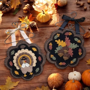 May include: Two felt Thanksgiving ornaments, one with a turkey and the other with acorns and leaves, hanging from black wire hangers with white and black ribbon bows.