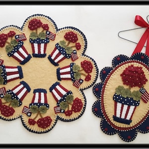 May include: Two felt wall hangings featuring red, white and blue geraniums in pots. The larger hanging is a round design with eight geraniums, while the smaller hanging is oval with one geranium. Both hangings have a scalloped edge and are decorated with blue and white stitching.