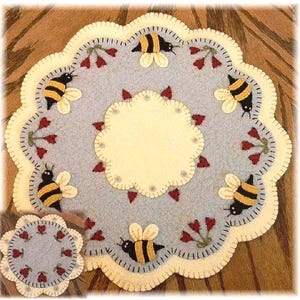 May include: A blue and cream felt rug with a scalloped edge. The rug features a central circle with a cream background and a blue border. The outer edge of the rug is decorated with red flowers and yellow bees.