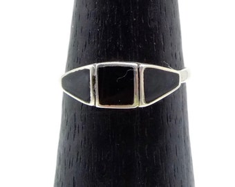 May include: A silver ring with a rectangular black stone in the center, flanked by two black trapezoid-shaped stones. The ring is displayed on a black, cone-shaped stand against a white background.