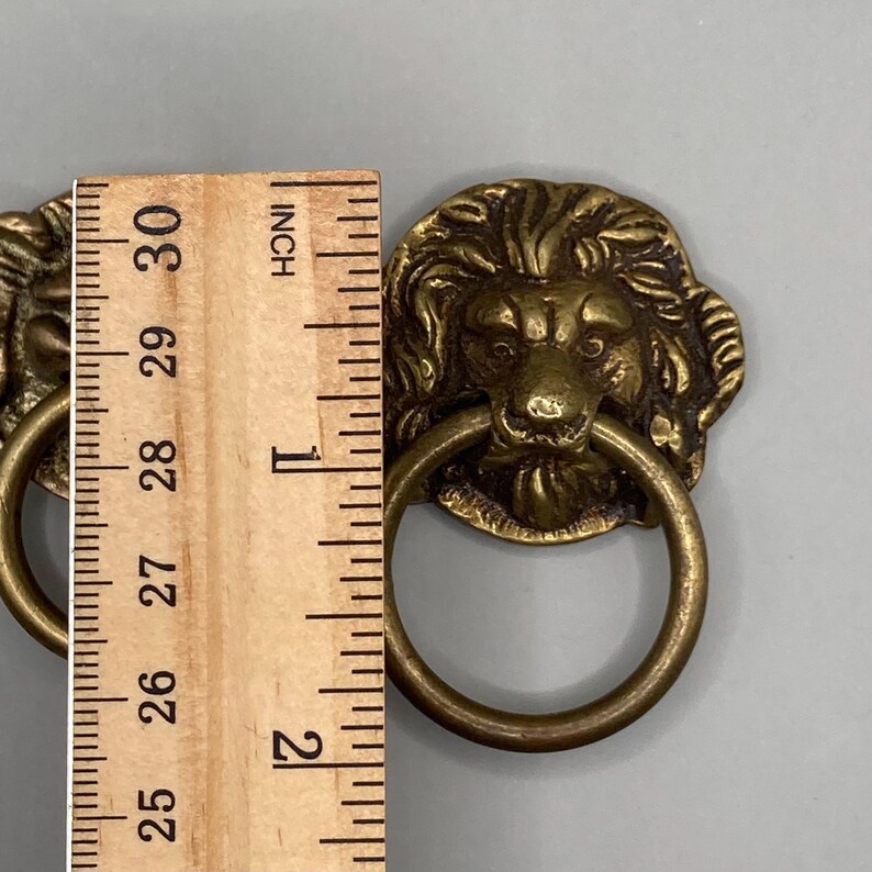 Puede incluir: Dos tiradores de cajones de cabeza de le&oacute;n de lat&oacute;n antiguo con asas de anillo. Cada tirador mide aproximadamente 2,5 cm de di&aacute;metro.