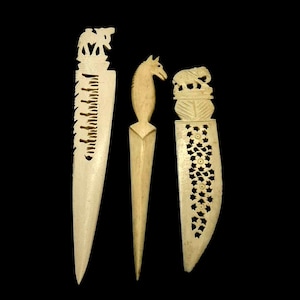 May include: Three off-white, carved letter openers. The left opener features an elephant topper and a serrated edge. The center opener is shaped like a horse head. The right opener displays an elephant topper and a floral cutout pattern.