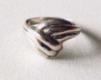 May include: A silver ring with a unique, abstract design. The ring is made of smooth, polished metal and has a curved, wave-like shape.