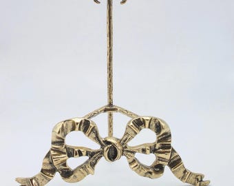 Peut inclure: Un présentoir en métal doré avec un motif de nœud. Le support a un support vertical avec un dessus décoratif et une base en forme de nœud. Le nœud présente des plis de ruban détaillés et un accent ovale central.