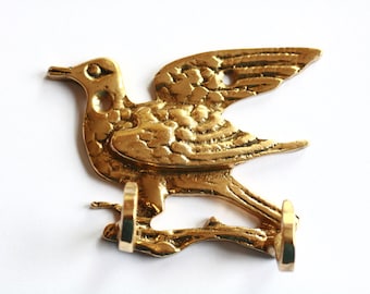 May include: Gold-toned metal bird hook with two hooks on the bottom. The bird is in flight with its wings spread out.