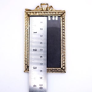 May include: A gold-colored picture frame with a decorative design around the edge. The frame is 4 inches tall and 3 inches wide.