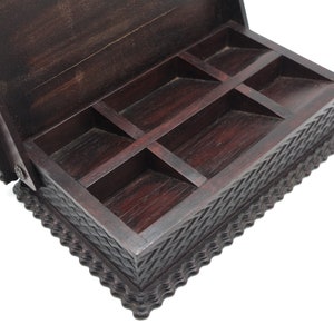 May include: A dark brown wooden box with a hinged lid and intricate carvings. The box has six compartments inside.