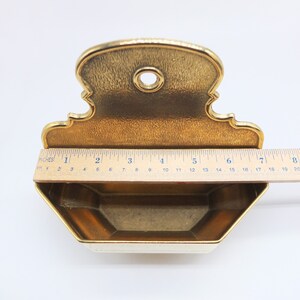 Puede incluir: Un jabonera de metal dorado con un dise&ntilde;o decorativo y ornamentado. La jabonera tiene una forma hexagonal y un peque&ntilde;o agujero en la parte posterior para colgar.