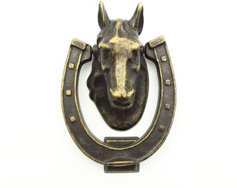 Puede incluir: Un llamador de puerta de bronce con forma de herradura y cabeza de caballo.