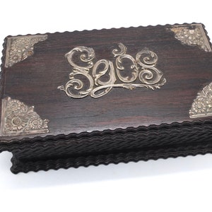 May include: A dark wood box with silver floral accents and the word "Sejos" engraved on the top.