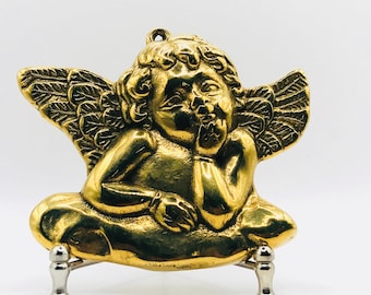Puede incluir: Una figurita de ángel querubín de oro con alas, sentada en un soporte. El ángel se está tocando la barbilla y tiene una expresión pensativa.