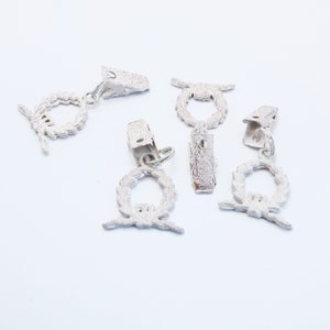 May include: Five white metal curtain tiebacks with a wreath design. Each tieback has a clip to hold the curtain in place.