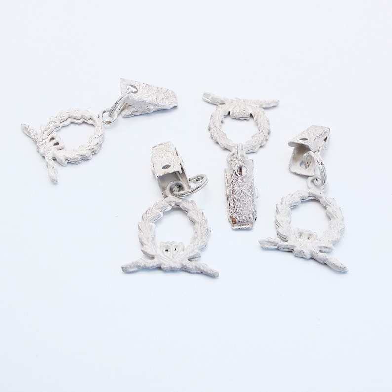 May include: Five white metal curtain tiebacks with a wreath design. Each tieback has a clip to hold the curtain in place.