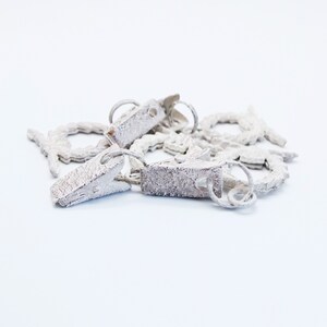 May include: A set of white metal curtain tiebacks with a decorative design. The tiebacks are connected by a chain and have a clip on one end.