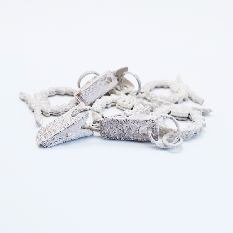 May include: A set of white metal curtain tiebacks with a decorative design. The tiebacks are connected by a chain and have a clip on one end.