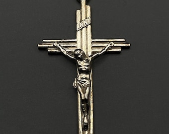 Puede incluir: Un colgante de crucifijo de metal plateado con un diseño de cruz texturizada de varias capas. La figura de Jesús está centrada en la cruz, con las letras INRI claramente grabadas en una pequeña placa colocada sobre la cabeza de la figura.