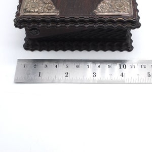 May include: A dark brown wooden box with a decorative silver top. The box is approximately 4 inches wide and 3 inches tall. The top of the box has a scalloped edge.
