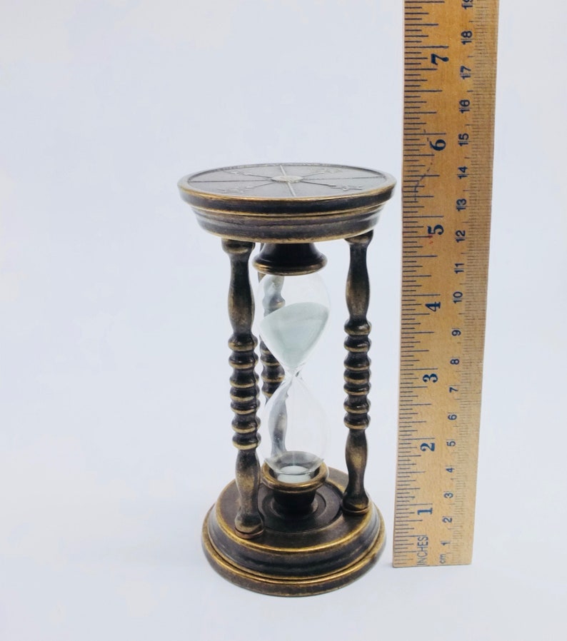 May include: A brass hourglass with a decorative base and a clear glass bulb. The hourglass is 6 inches tall.