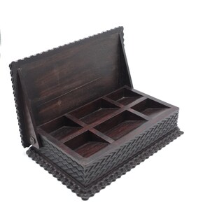 May include: A dark brown wooden box with a hinged lid and six compartments. The box has intricate carvings around the edges and a woven pattern on the bottom.
