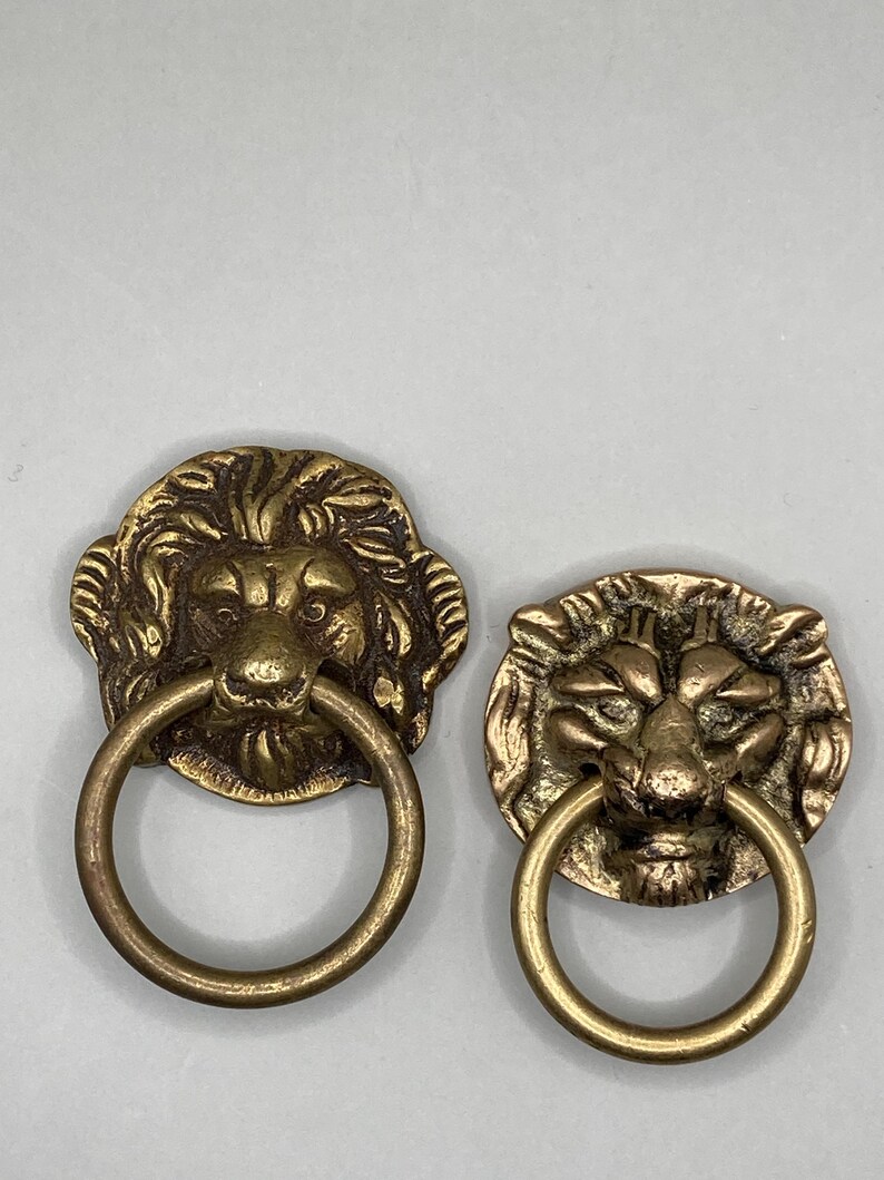 Puede incluir: Dos pomos de puerta antiguos de lat&oacute;n en forma de cabeza de le&oacute;n con tiradores de anillo. Las cabezas de le&oacute;n est&aacute;n detalladas con pelo texturizado y tienen una expresi&oacute;n realista.