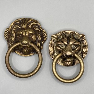 Puede incluir: Dos pomos de puerta antiguos de lat&oacute;n en forma de cabeza de le&oacute;n con tiradores de anillo. Las cabezas de le&oacute;n est&aacute;n detalladas con pelo texturizado y tienen un aspecto realista.