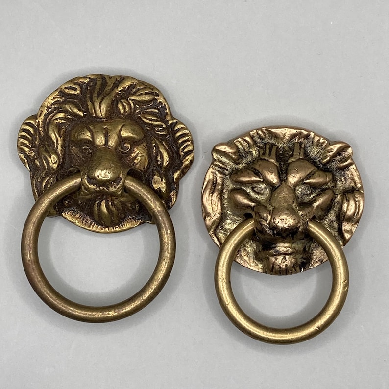 Puede incluir: Dos pomos de puerta antiguos de lat&oacute;n en forma de cabeza de le&oacute;n con tiradores de anillo. Las cabezas de le&oacute;n est&aacute;n detalladas con pelo texturizado y tienen un aspecto realista.