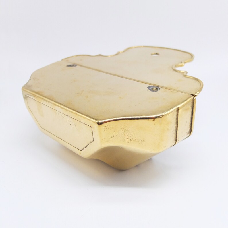 Puede incluir: Una caja de metal de color dorado con forma de viol&iacute;n. La caja est&aacute; cerrada y tiene una peque&ntilde;a etiqueta rectangular en la parte inferior.