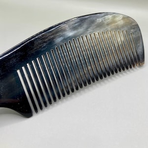 May include: A black and white horn comb with a curved handle. The comb has fine teeth and is made of natural horn.