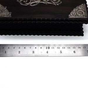 May include: A dark wood box with silver floral accents and a decorative design on the top. The box is approximately 8 inches long.