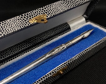 May include: A silver pen with an ornate design and a pointed nib, resting in a black and white patterned box with a blue lining.