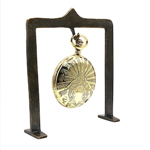 May include: A gold pocket watch with an intricate design on the face is displayed on a metal stand.