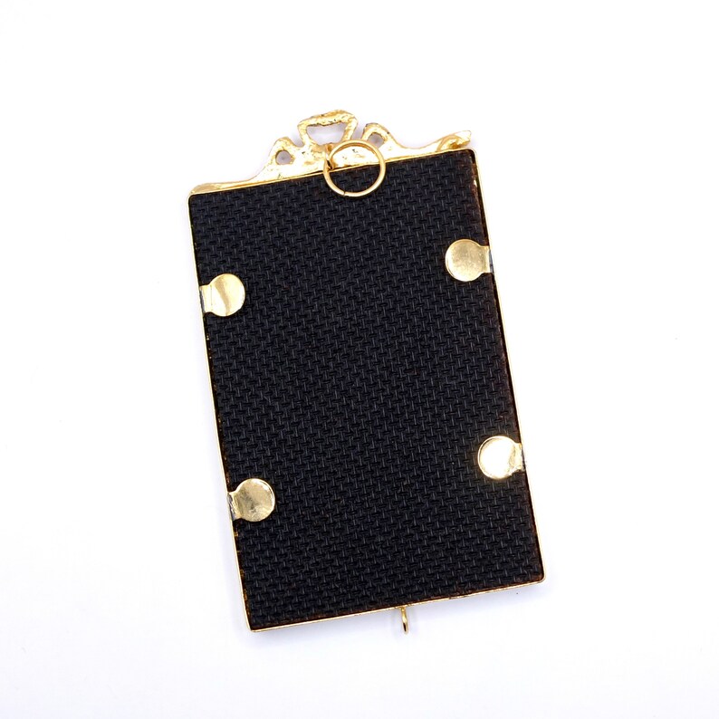 May include: A gold-colored picture frame with a black fabric backing and four gold-colored accents. The frame has a decorative top with a ring.