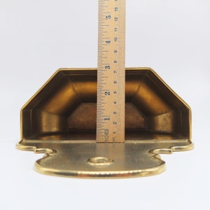 Puede incluir: Un estante de pared de metal dorado con un dise&ntilde;o decorativo. El estante mide aproximadamente 15 cm de alto.