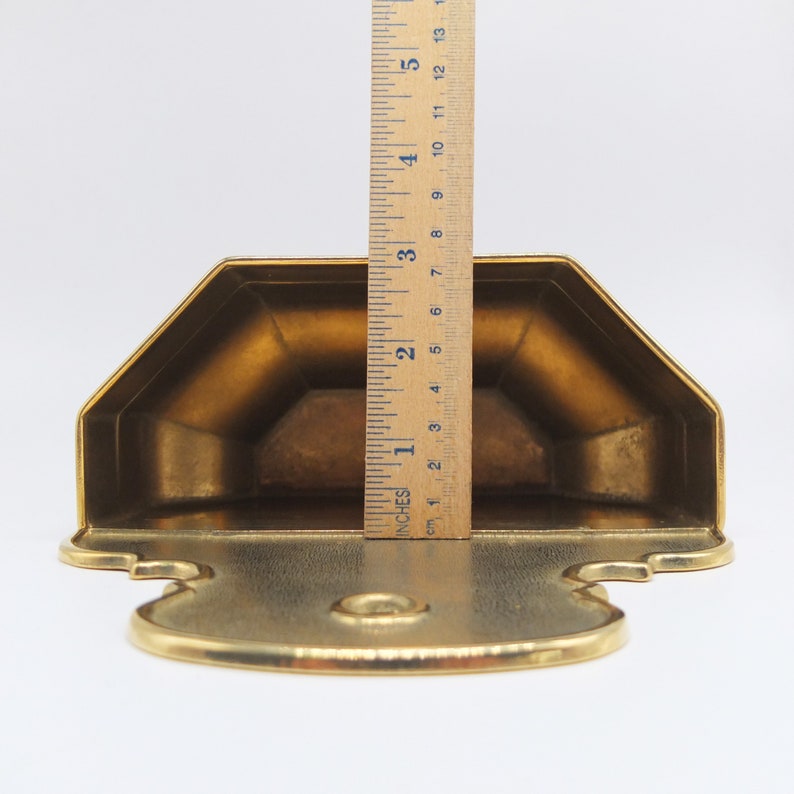 Puede incluir: Un estante de pared de metal dorado con un dise&ntilde;o decorativo. El estante mide aproximadamente 15 cm de alto.