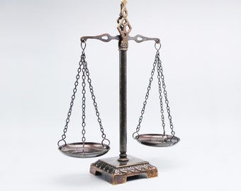 May include: A decorative antique-style scale with two metal bowls hanging from chains. The scale is made of brass and has an ornate design. The scale is balanced and ready to weigh.