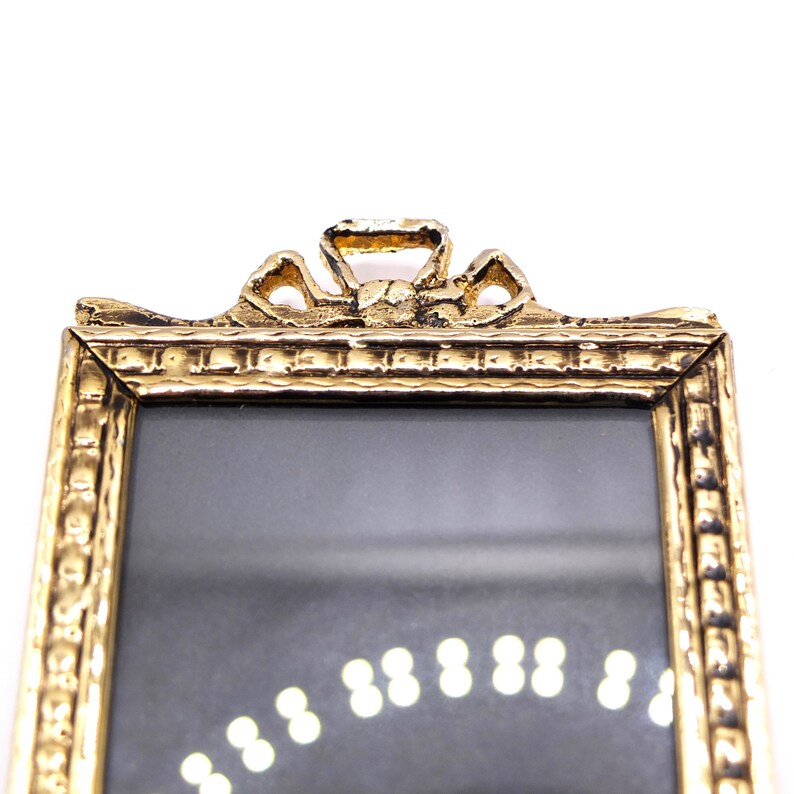 May include: A gold-colored picture frame with a decorative, ornate top. The frame has a rectangular shape and a smooth, reflective surface.