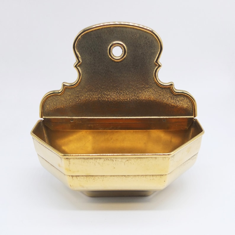 Puede incluir: Un plato decorativo de pared de color dorado con un borde festoneado y una parte superior elevada y adornada.