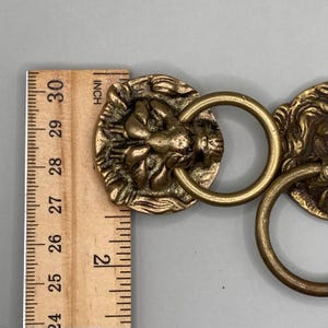 Puede incluir: Dos pomos de puerta de lat&oacute;n con forma de cabeza de le&oacute;n con anillos. Los pomos miden aproximadamente 5 cm de di&aacute;metro.