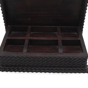 May include: A dark brown wooden box with a carved design and a hinged lid. The box has six compartments inside.