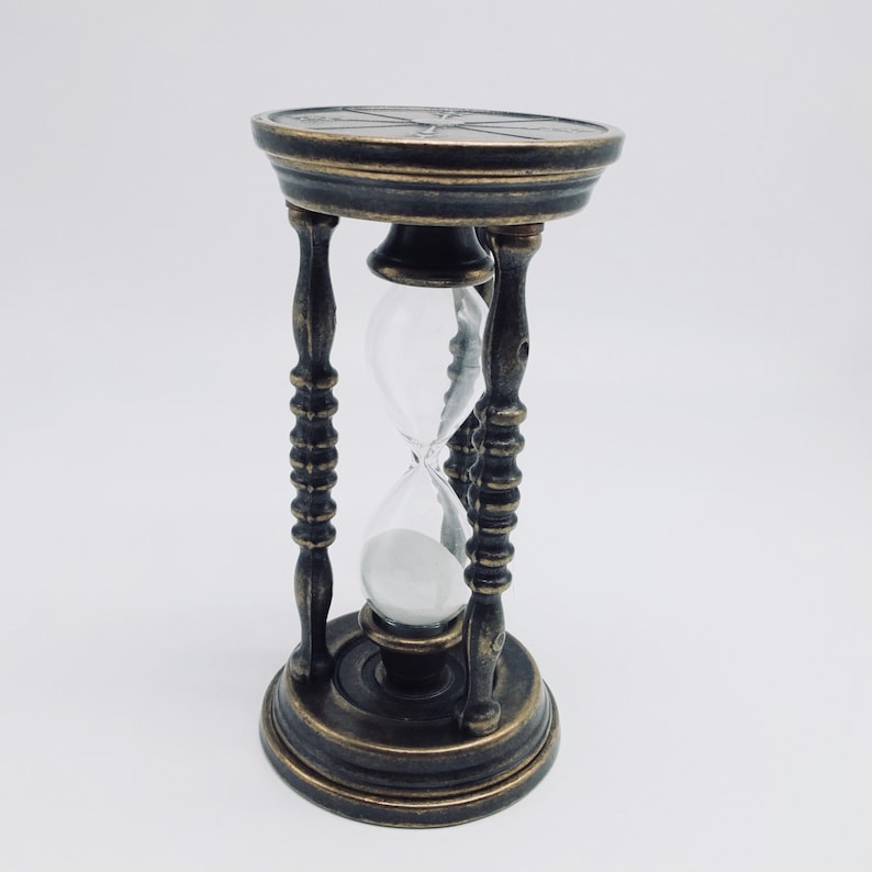 May include: A brass hourglass with a black and gold finish. The hourglass is filled with sand and has a decorative top.