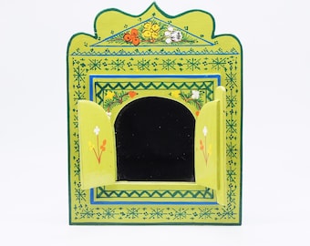 Puede incluir: Una pequeña caja de madera verde con un espejo en su interior. La caja está decorada con flores pintadas y un patrón geométrico.