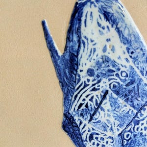 May include: Close-up of a blue and white ceramic piece with intricate patterns. The design features a combination of swirling lines and geometric shapes. The piece is set against a beige background.