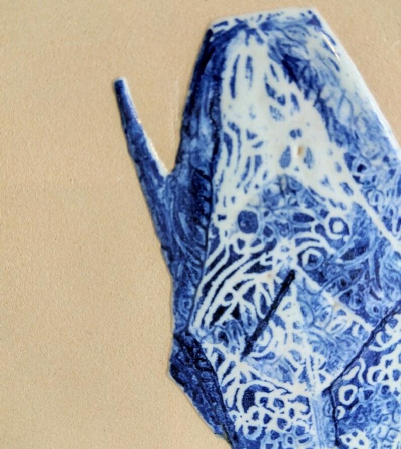 May include: Close-up of a blue and white ceramic piece with intricate patterns. The design features a combination of swirling lines and geometric shapes. The piece is set against a beige background.